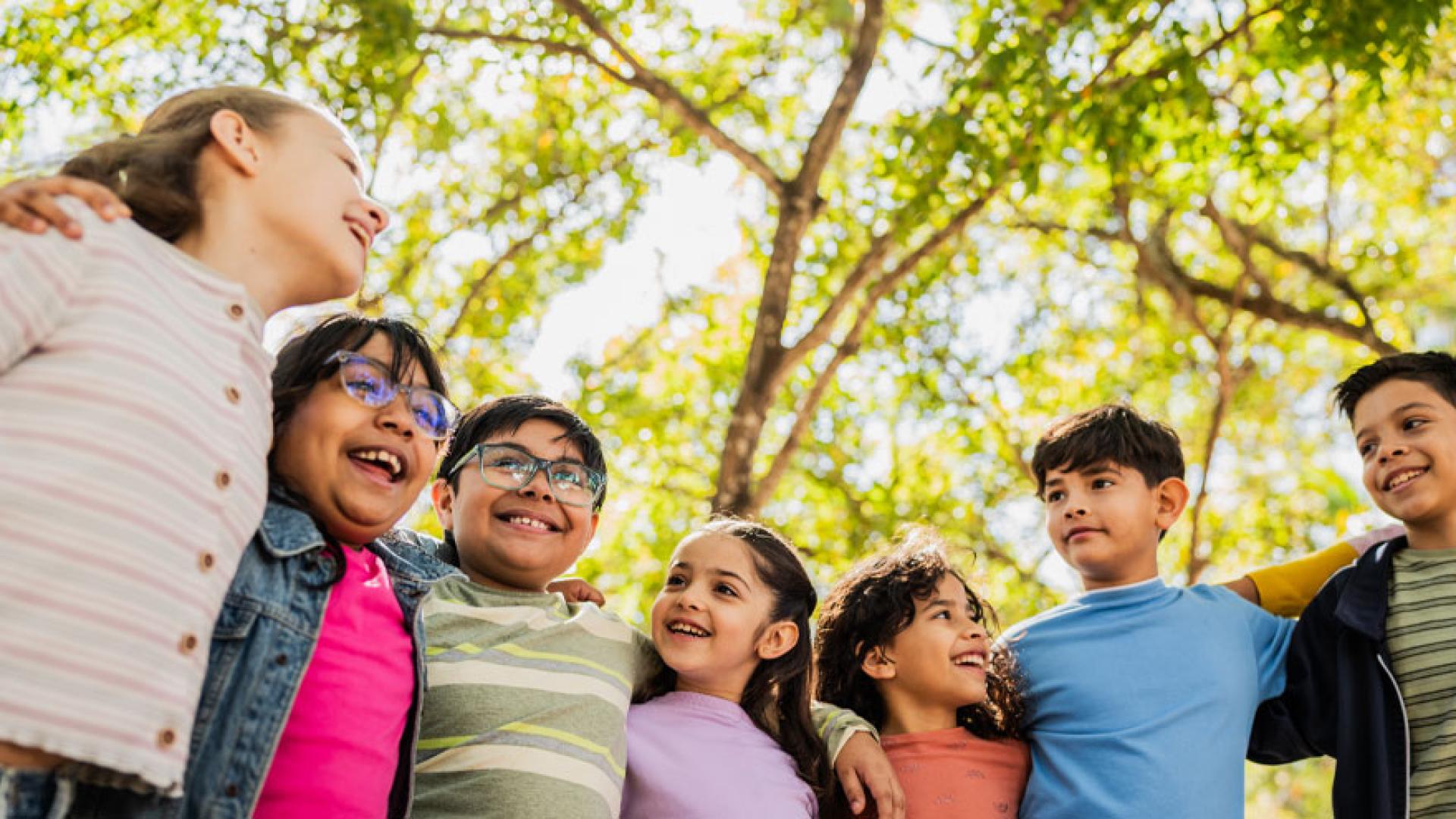 Child friends embrace shouder to shoulder, smiling in a sunny outdoor natural setting