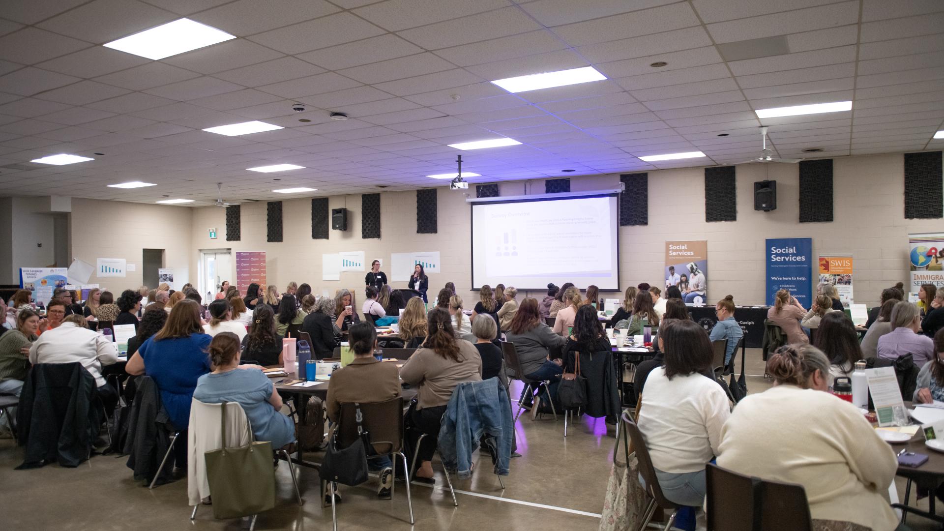 A group of people sitting at banquet tables listening to a presentation. 