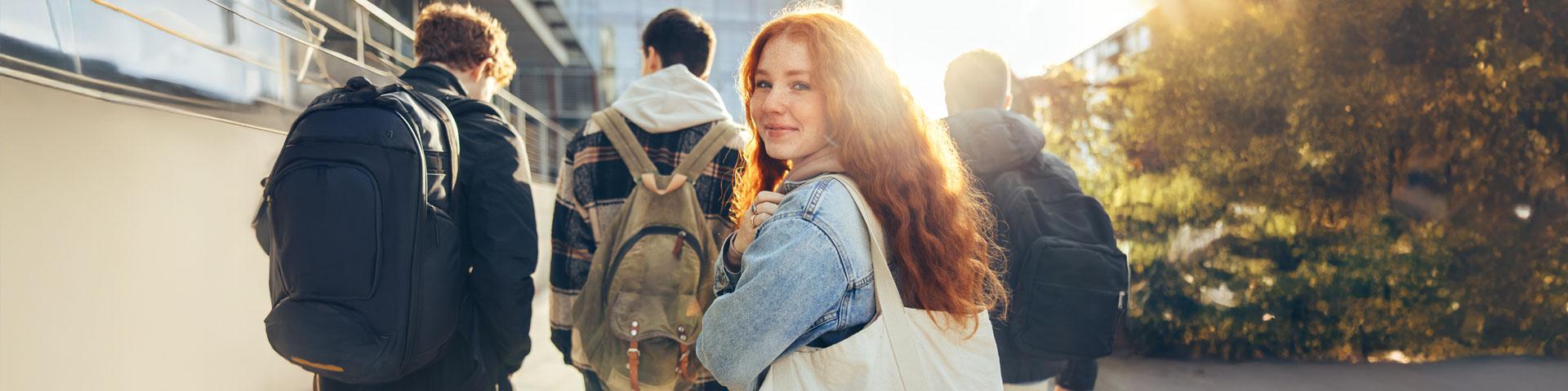 Female teen student glancing back while going for a class, walking with friends.